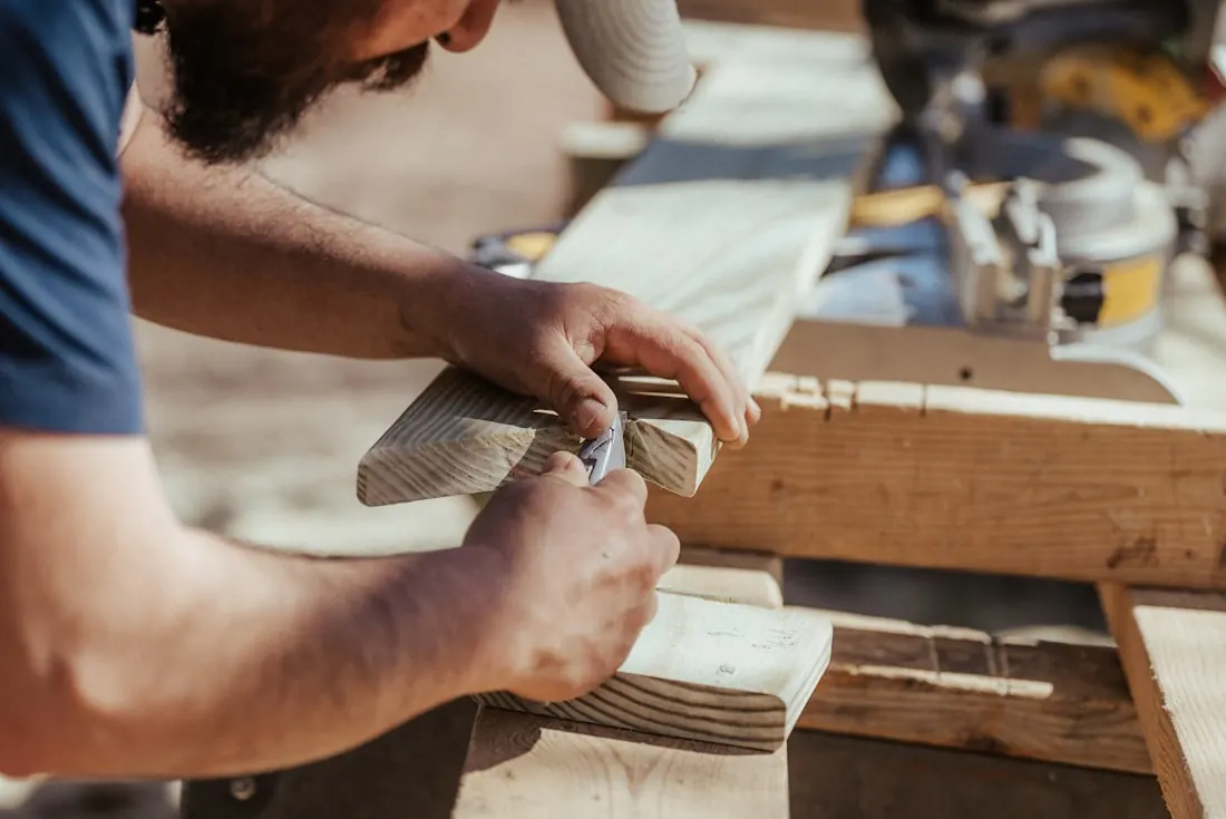 Un artisan marque une pièce de bois au crayon, scie à onglets en arrière-plan